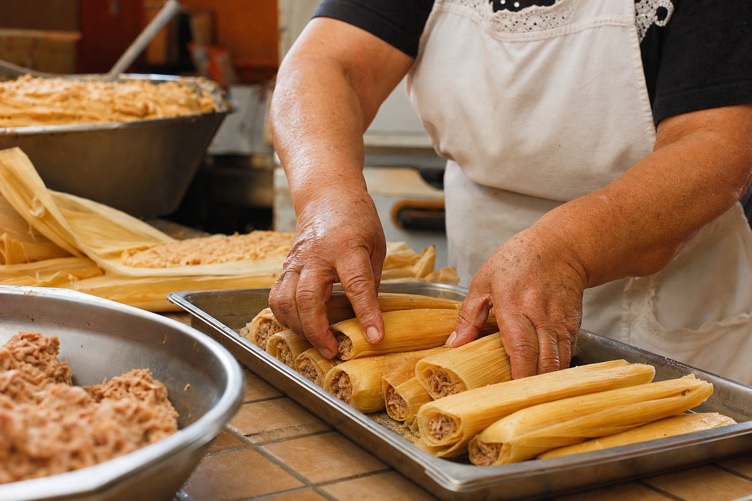 Hands arranging handmade tamales on a tray